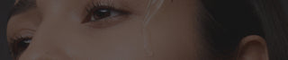 A close-up of a woman’s face as a dropper applies a clear liquid skincare serum beneath her eye.