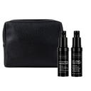 The Revision Skincare Healthy Glow Power Duo features two black bottles standing upright in front of a textured black pouch on a white background.