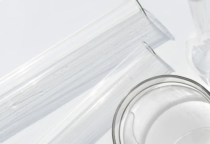 Clear laboratory glassware, including test tubes and a beaker filled with liquid, arranged on a white surface with light reflections.