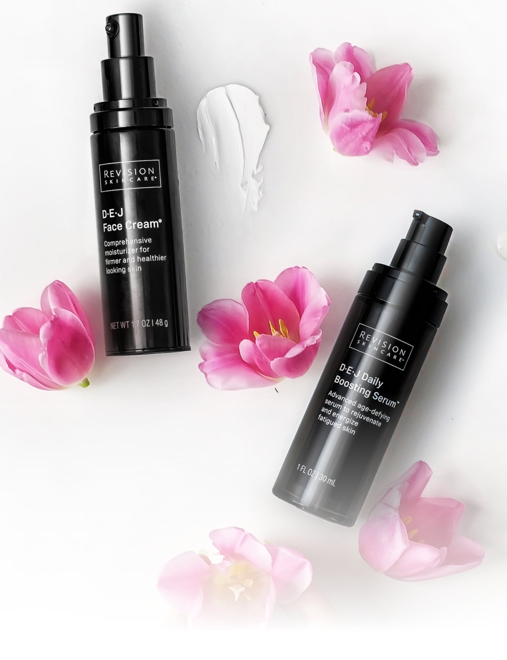 Two black bottles of Revision Skincare products lie on a white surface with pink flowers and a smear of white cream. The labels read DEJ Face Cream and DEJ Daily Boosting Serum.