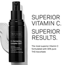 A black bottle of Revision Skincare Healthy Glow Power Duo stands upright, emphasizing its Vitamin C treatment for radiant skin, as a white ceramic hand gently holds the product.