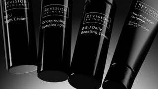Four black skincare product bottles from Revision Skincare are shown against a dark background. Visible labels include DEJ Night Cream, C+ Correcting Complex 30%, DEJ Daily Boosting Serum, and Intellishade Original SPF 45.