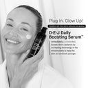 A smiling woman in a white robe applies cream to her cheek while holding a bottle of Revision Skincare’s D·E·J Daily Boosting Serum® 2 fl oz, an anti-aging serum that enhances skin radiance and firmness.
