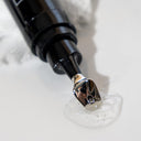 A close-up of a black and silver pump dispensing clear Revox™ Line Relaxer gel by Revision Skincare onto a white surface, with a crumpled white cloth in the background—ideal for your fine line and wrinkle care routine.