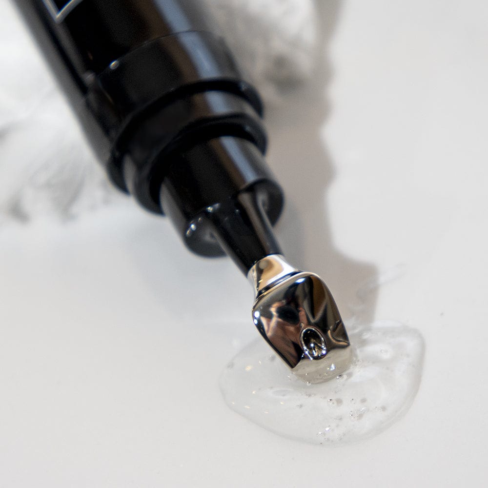 A close-up of a black and silver pump dispensing clear Revox™ Line Relaxer gel by Revision Skincare onto a white surface, with a crumpled white cloth in the background—ideal for your fine line and wrinkle care routine.