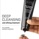 A hand squeezes a black tube of Revision Skincare Pore Purifying Clay Mask, releasing gray cream, as text highlights its ability to unclog and refine pores for a smoother-looking complexion.