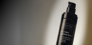 A black pump bottle labeled Revision Skincare DEJ Daily Boosting Serum, described as an advanced age-defying serum to rejuvenate and energize fatigued skin, is shown against a blurred gradient background.