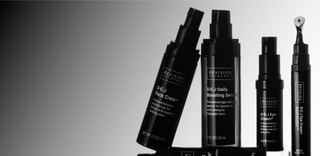 Five black skincare product bottles and tubes from Revision Skincare are displayed on a gradient black-to-white background, standing upright with labels visible, including face cream, serums, and eye cream.