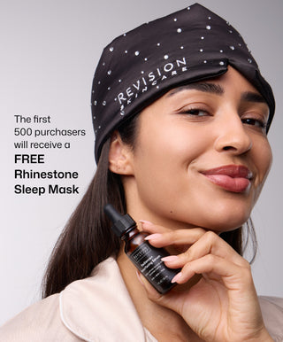 A woman wearing a black rhinestone sleep mask holds Revision Skincare Radiance+ Resurfacing Serum and smiles. Text: The first 500 purchasers get a FREE Rhinestone Sleep Mask—perfect for your overnight treatment routine!.