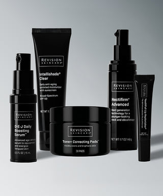 Five skincare products from The Tone-Perfecting Collection in black packaging: a serum pump, a moisturizer tube, a jar of tone correcting pads, a neck pump bottle, and a small lip treatment tube for a brighter, even-toned complexion.