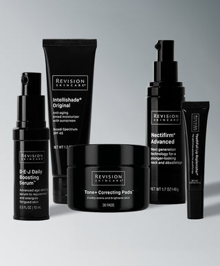 The Tone-Perfecting Collection by Revision Skincare, featuring five black products: a brightening serum bottle, moisturizer tube, jar of correcting pads, pump bottle, and lip treatment tube.