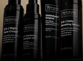 Four black bottles of Revision Skincare products, including D·E·J Night Face Cream, C+ Correcting Complex 30%, Intellishade Original SPF 45, and D·E·J Daily Boosting Serum, are arranged closely together.