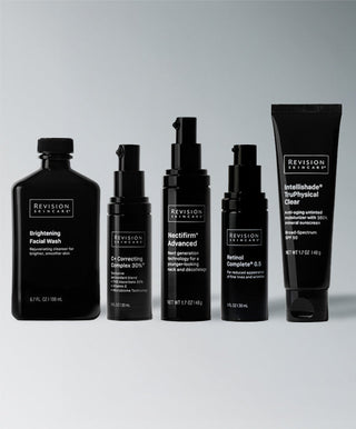 Five black bottles and tubes from Revision Skincare's Brightening Full Size Regimen are arranged in a row on a light gray background, featuring products designed to help brighten and even skin tone.