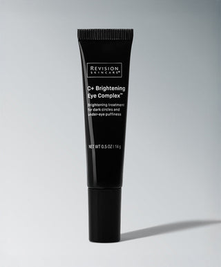 A black tube of Revision Skincare C+ Brightening Eye Complex™ stands upright on a light gray background. This Vitamin C eye complex targets dark circles and under-eye puffiness.