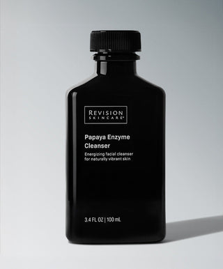 A black bottle of Revision Skincare Papaya Enzyme Cleanser, 3.4 fl oz (100 mL), with white text sits on a gray background; this enzyme-based cleanser uses Papaya Fruit Extract for naturally radiant skin.