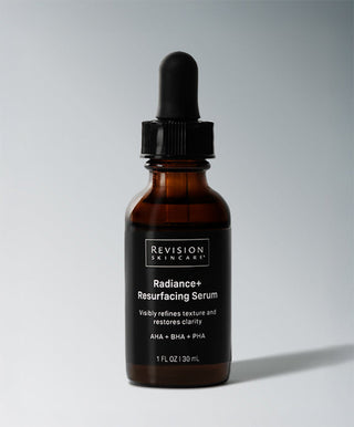 A brown glass dropper bottle labeled Radiance+ Resurfacing Serum by Revision Skincare, shown against a light background, highlights an overnight treatment that visibly refines skin texture and restores clarity with AHA, BHA & PHA. 1 fl oz (30 mL).