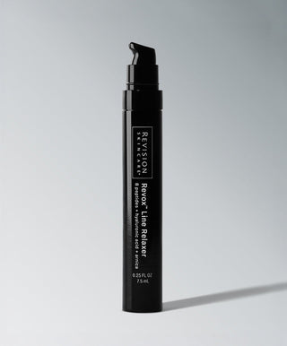 A black cylindrical bottle with a pump, labeled Revision Skincare Revox™ Line Relaxer, stands upright on a light gray surface with a soft shadow—an advanced serum designed to target wrinkles.