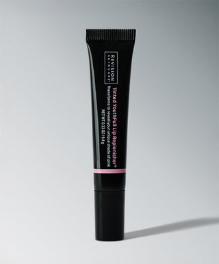 A black tube of Revision Skincare Tinted YouthFull Lip Replenisher® stands upright on a gray background, with white and pink text highlighting this age-defying lip treatment and its size.