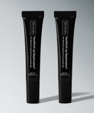 Two black tubes of Revision Skincare YouthFull Lip Replenisher®, each 0.33 oz, stand upright on a gray surface against a light gray background.
